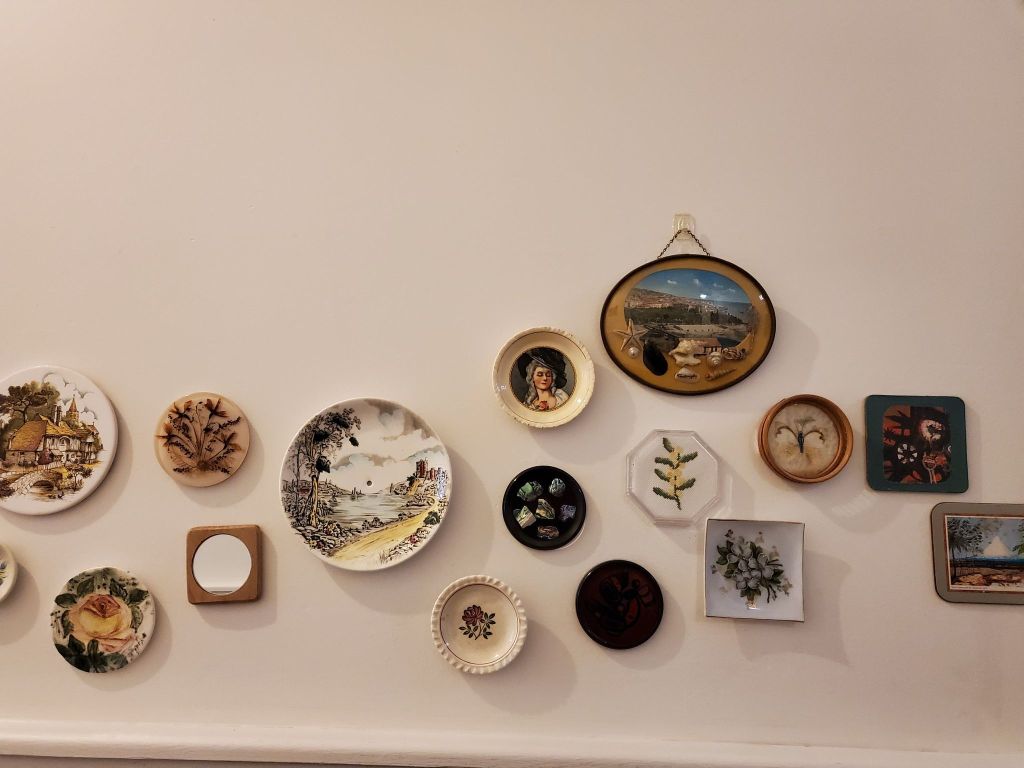 A wall of ye olde English wall plates, painings and embroideries